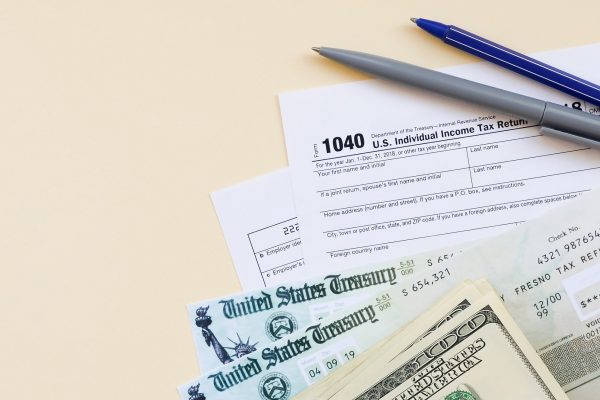 1040 Individual Income tax return form with Refund Check and hundred dollar bills on beige